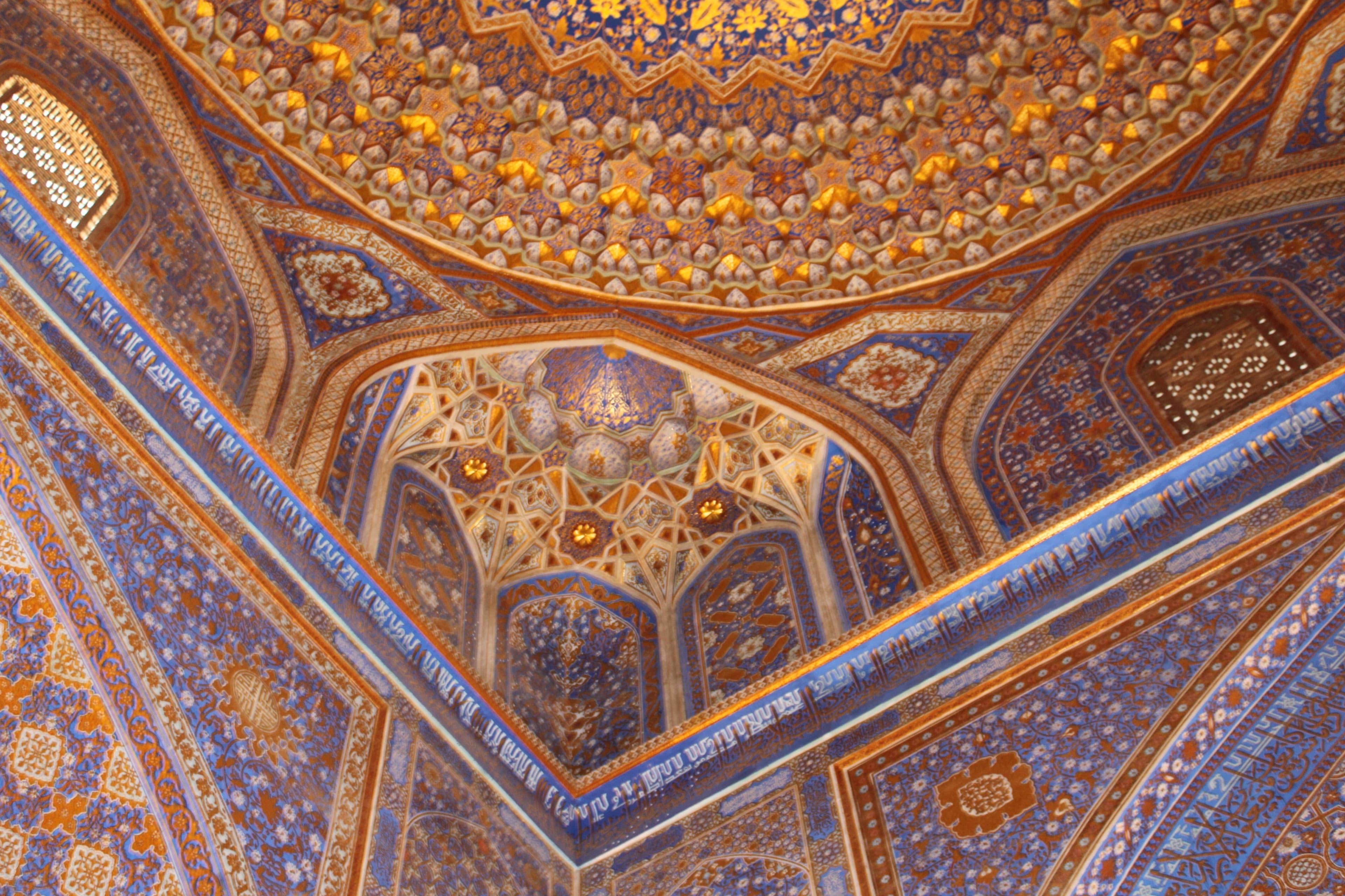 Tiered niches at the edge of the Tilya-Kori prayer hall dome, with corner transitions and a calligraphic band